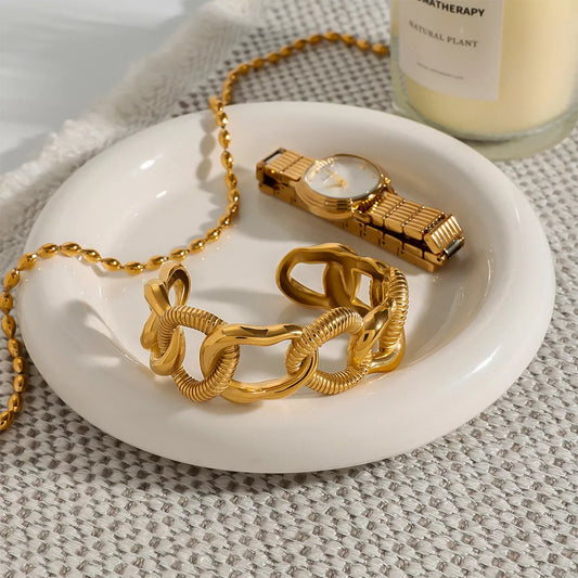 18K gold-plated chain link open bracelet on white dish with gold watch and candle